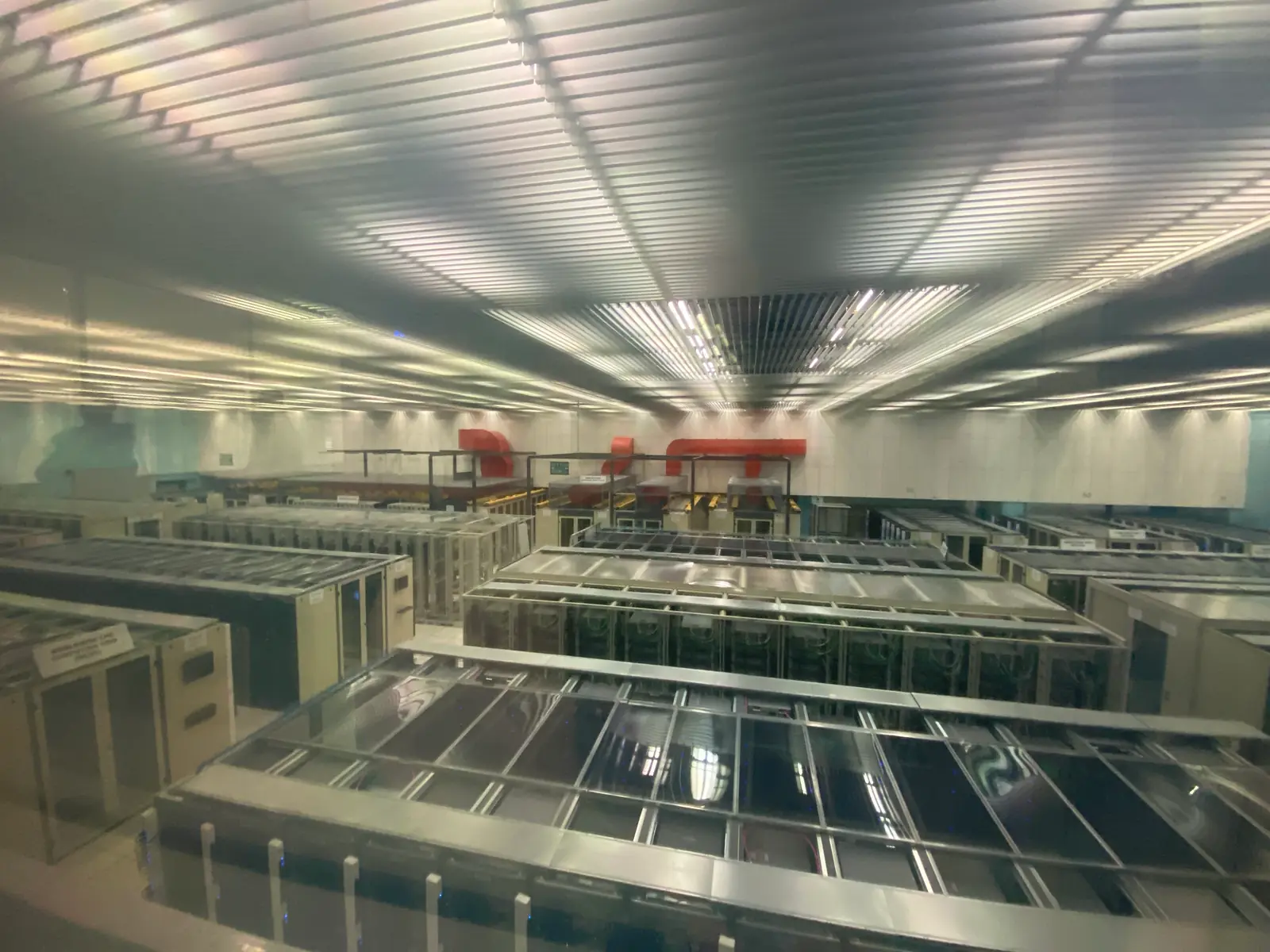Long rows of low server cabinets under a bright ribbed ceiling, receding to the far wall of a data hall.