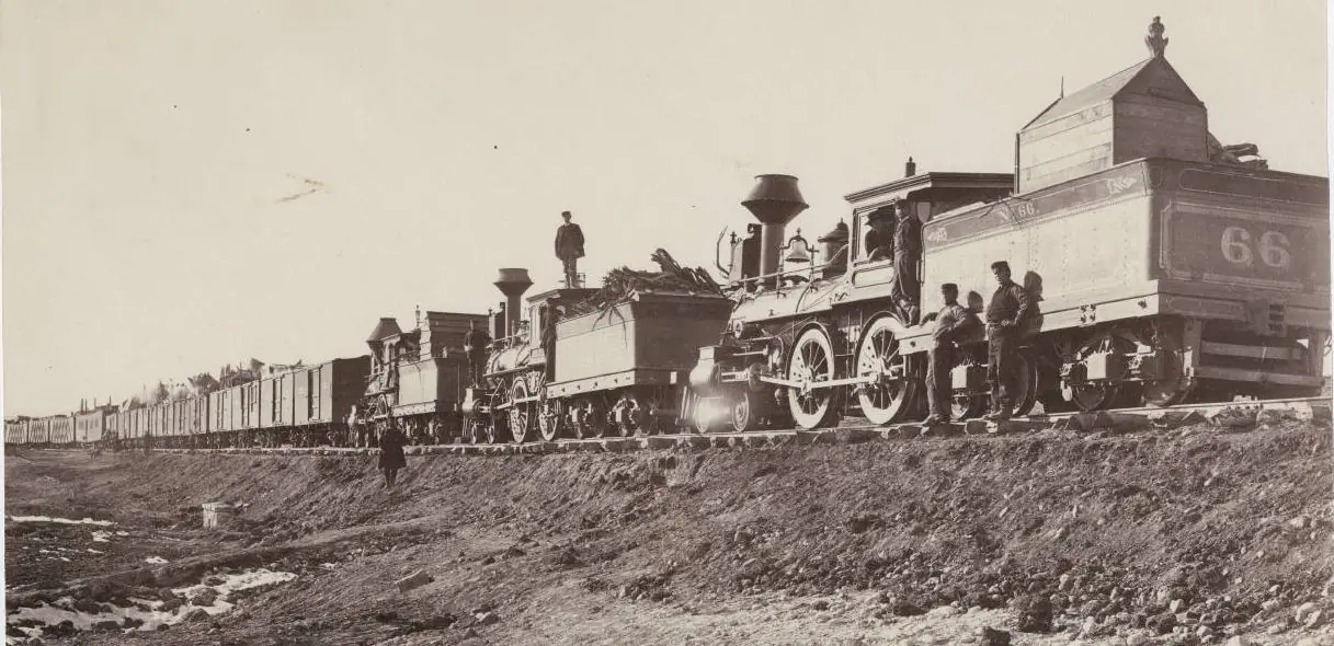 A Union Pacific locomotive and its crew standing on a raw, unballasted graded embankment, construction cars stretching back along the advancing line under construction.